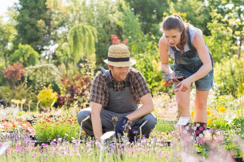 Community gardener kneeling beside pathway with tools in Seven Kings garden